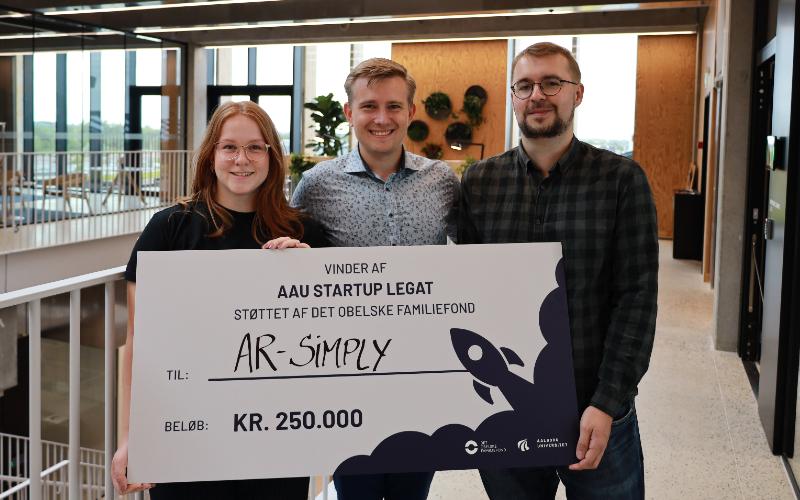 Nanna Heidemann Jensen, Frederik Nørgaard Jensen, and Tobias Harpøth Adamsen proudly showcase their AAU Startup Grant.